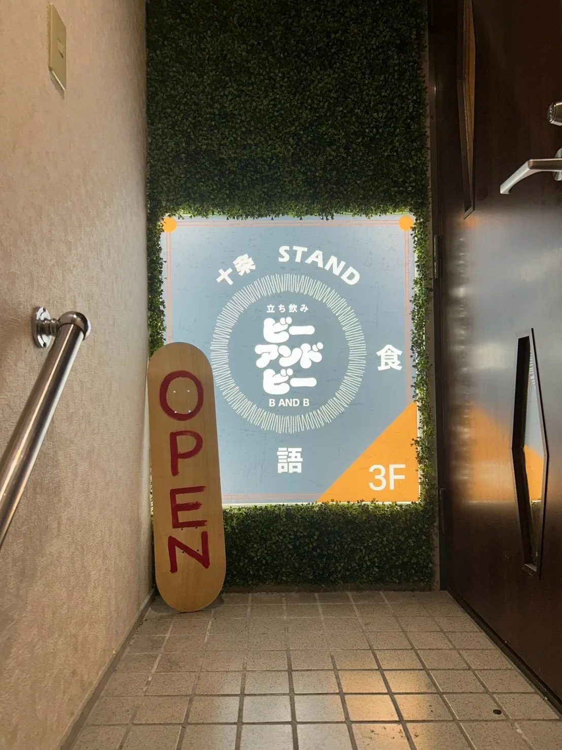 緑の壁に掲げた十条STAND B&Bの看板。立ち飲み、3階。